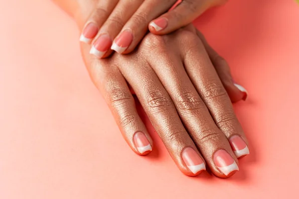 Stylish trendy french manicure. Hands of a beautiful young woman are covered by highlight on a pink background.