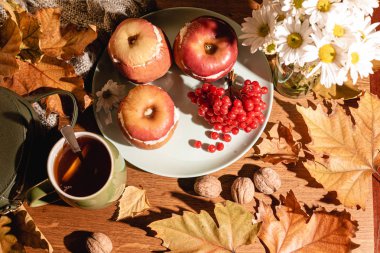 Sonbahar kompozisyonu. Peynirli fırınlanmış elma, kızılcık, çay ve yapraklar masanın üstünde..