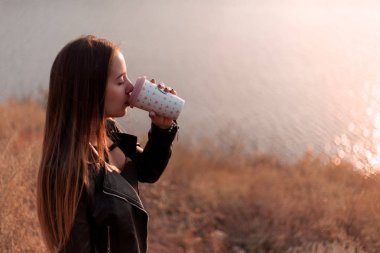 Kız doğada kahve içer. Sonbahar günü, gün batımı.