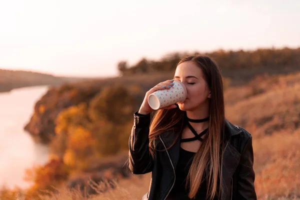 Girl drinks coffee on the nature. Autumn day, sunset.