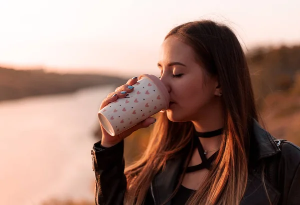 Girl drinks coffee on the nature. Autumn day, sunset.