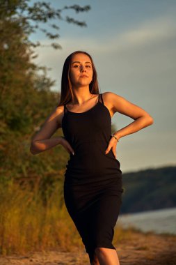 Yeşil sahil yakınında doğada güzel bir kız. Batan güneşin tadını çıkarıyor. Açık hava eğlencesi konsepti, parkta yürüyüş. Şehrin telaşından dolayı gevşeme.