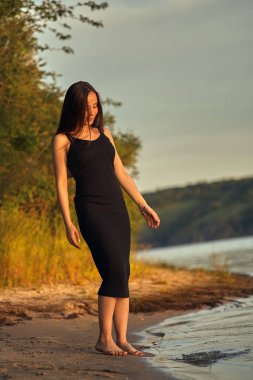 Yeşil sahil yakınında doğada güzel bir kız. Batan güneşin tadını çıkarıyor. Açık hava eğlencesi konsepti, parkta yürüyüş. Şehrin telaşından dolayı gevşeme.