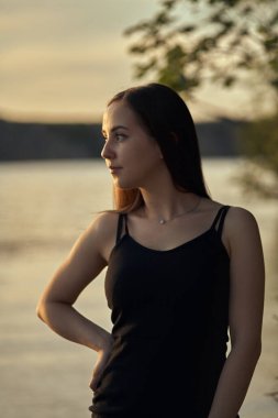 Yeşil sahil yakınında doğada güzel bir kız. Batan güneşin tadını çıkarıyor. Açık hava eğlencesi konsepti, parkta yürüyüş. Şehrin telaşından dolayı gevşeme.