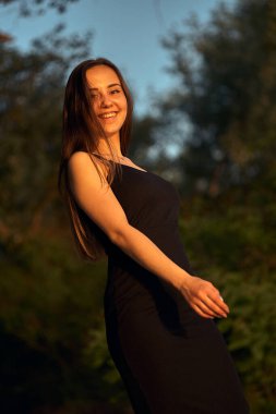 Yeşil sahil yakınında doğada güzel bir kız. Batan güneşin tadını çıkarıyor. Açık hava eğlencesi konsepti, parkta yürüyüş. Şehrin telaşından dolayı gevşeme.