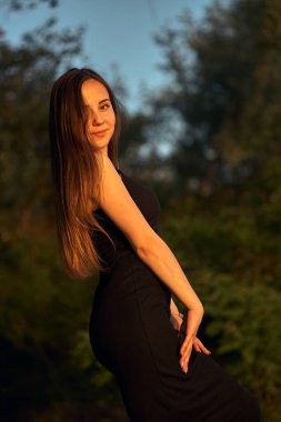 Yeşil sahil yakınında doğada güzel bir kız. Batan güneşin tadını çıkarıyor. Açık hava eğlencesi konsepti, parkta yürüyüş. Şehrin telaşından dolayı gevşeme.