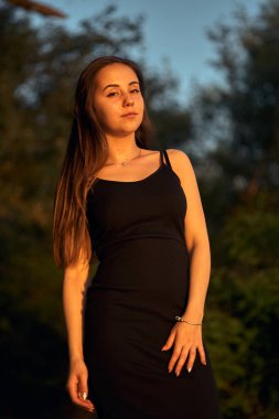 Yeşil sahil yakınında doğada güzel bir kız. Batan güneşin tadını çıkarıyor. Açık hava eğlencesi konsepti, parkta yürüyüş. Şehrin telaşından dolayı gevşeme.