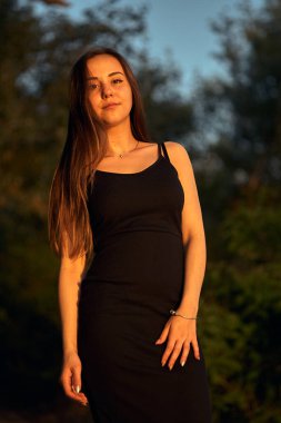 Yeşil sahil yakınında doğada güzel bir kız. Batan güneşin tadını çıkarıyor. Açık hava eğlencesi konsepti, parkta yürüyüş. Şehrin telaşından dolayı gevşeme.