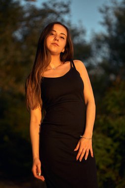 Yeşil sahil yakınında doğada güzel bir kız. Batan güneşin tadını çıkarıyor. Açık hava eğlencesi konsepti, parkta yürüyüş. Şehrin telaşından dolayı gevşeme.