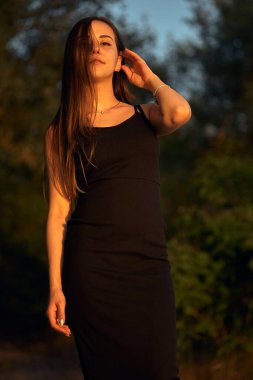 Yeşil sahil yakınında doğada güzel bir kız. Batan güneşin tadını çıkarıyor. Açık hava eğlencesi konsepti, parkta yürüyüş. Şehrin telaşından dolayı gevşeme.