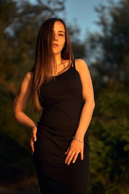 Yeşil sahil yakınında doğada güzel bir kız. Batan güneşin tadını çıkarıyor. Açık hava eğlencesi konsepti, parkta yürüyüş. Şehrin telaşından dolayı gevşeme.