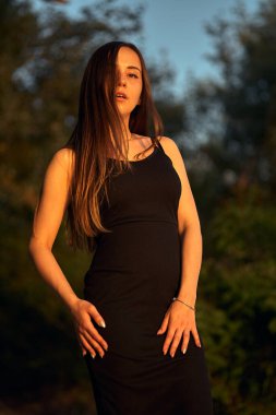 Yeşil sahil yakınında doğada güzel bir kız. Batan güneşin tadını çıkarıyor. Açık hava eğlencesi konsepti, parkta yürüyüş. Şehrin telaşından dolayı gevşeme.