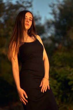 Yeşil sahil yakınında doğada güzel bir kız. Batan güneşin tadını çıkarıyor. Açık hava eğlencesi konsepti, parkta yürüyüş. Şehrin telaşından dolayı gevşeme.