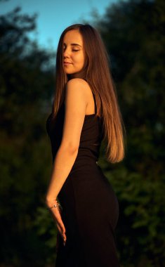 Yeşil sahil yakınında doğada güzel bir kız. Batan güneşin tadını çıkarıyor. Açık hava eğlencesi konsepti, parkta yürüyüş. Şehrin telaşından dolayı gevşeme.