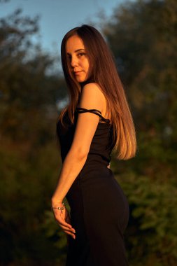 Yeşil sahil yakınında doğada güzel bir kız. Batan güneşin tadını çıkarıyor. Açık hava eğlencesi konsepti, parkta yürüyüş. Şehrin telaşından dolayı gevşeme.