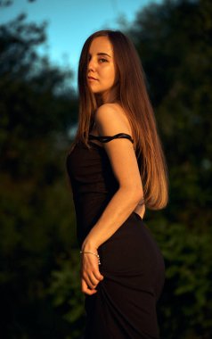 Yeşil sahil yakınında doğada güzel bir kız. Batan güneşin tadını çıkarıyor. Açık hava eğlencesi konsepti, parkta yürüyüş. Şehrin telaşından dolayı gevşeme.