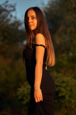 Yeşil sahil yakınında doğada güzel bir kız. Batan güneşin tadını çıkarıyor. Açık hava eğlencesi konsepti, parkta yürüyüş. Şehrin telaşından dolayı gevşeme.