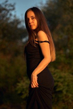 Yeşil sahil yakınında doğada güzel bir kız. Batan güneşin tadını çıkarıyor. Açık hava eğlencesi konsepti, parkta yürüyüş. Şehrin telaşından dolayı gevşeme.