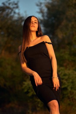 Yeşil sahil yakınında doğada güzel bir kız. Batan güneşin tadını çıkarıyor. Açık hava eğlencesi konsepti, parkta yürüyüş. Şehrin telaşından dolayı gevşeme.