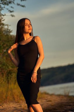 Yeşil sahil yakınında doğada güzel bir kız. Batan güneşin tadını çıkarıyor. Açık hava eğlencesi konsepti, parkta yürüyüş. Şehrin telaşından dolayı gevşeme.