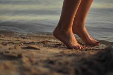 Sudaki kumlu bir sahilde çıplak ayaklı bir kadın. Güzel kadın bacaklarına yakın çekim. Islak ayak.