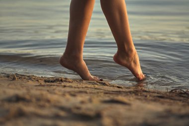 Sudaki kumlu bir sahilde çıplak ayaklı bir kadın. Güzel kadın bacaklarına yakın çekim. Islak ayak.