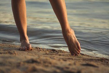 Sudaki kumlu bir sahilde çıplak ayaklı bir kadın. Güzel kadın bacaklarına yakın çekim. Islak ayak.