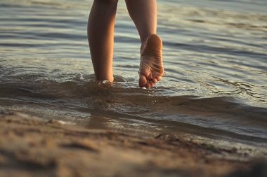 Sudaki kumlu bir sahilde çıplak ayaklı bir kadın. Güzel kadın bacaklarına yakın çekim. Islak ayak.