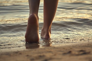 Sudaki kumlu bir sahilde çıplak ayaklı bir kadın. Güzel kadın bacaklarına yakın çekim. Islak ayak.