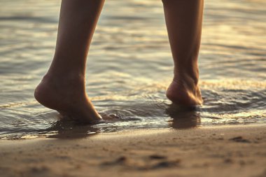 Sudaki kumlu bir sahilde çıplak ayaklı bir kadın. Güzel kadın bacaklarına yakın çekim. Islak ayak.