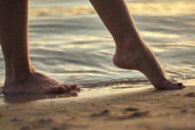 Sudaki kumlu bir sahilde çıplak ayaklı bir kadın. Güzel kadın bacaklarına yakın çekim. Islak ayak.