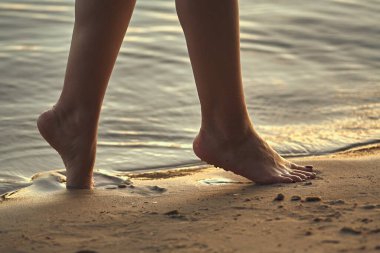 Sudaki kumlu bir sahilde çıplak ayaklı bir kadın. Güzel kadın bacaklarına yakın çekim. Islak ayak.