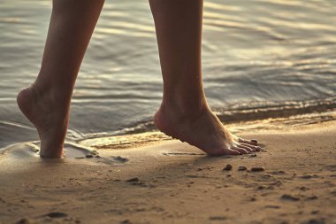 Sudaki kumlu bir sahilde çıplak ayaklı bir kadın. Güzel kadın bacaklarına yakın çekim. Islak ayak.