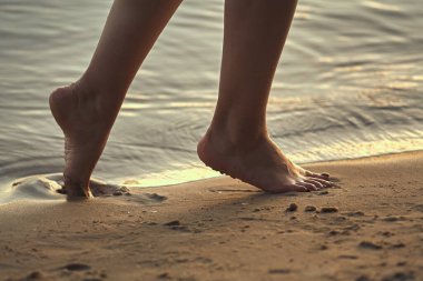 Sudaki kumlu bir sahilde çıplak ayaklı bir kadın. Güzel kadın bacaklarına yakın çekim. Islak ayak.