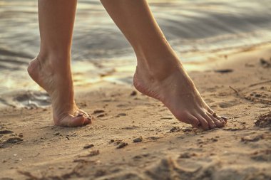 Sudaki kumlu bir sahilde çıplak ayaklı bir kadın. Güzel kadın bacaklarına yakın çekim. Islak ayak.
