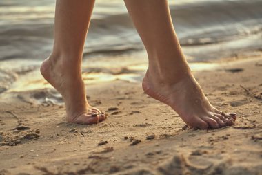 Sudaki kumlu bir sahilde çıplak ayaklı bir kadın. Güzel kadın bacaklarına yakın çekim. Islak ayak.