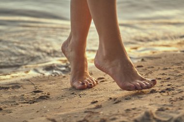 Sudaki kumlu bir sahilde çıplak ayaklı bir kadın. Güzel kadın bacaklarına yakın çekim. Islak ayak.