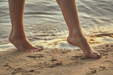 Sudaki kumlu bir sahilde çıplak ayaklı bir kadın. Güzel kadın bacaklarına yakın çekim. Islak ayak.