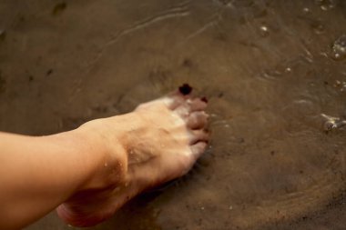 Sudaki kumlu bir sahilde çıplak ayaklı bir kadın. Güzel kadın bacaklarına yakın çekim. Islak ayak.