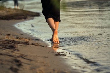 Sudaki kumlu bir sahilde çıplak ayaklı bir kadın. Güzel kadın bacaklarına yakın çekim. Islak ayak.