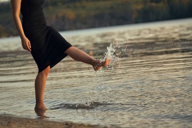 Sudaki kumlu bir sahilde çıplak ayaklı bir kadın. Güzel kadın bacaklarına yakın çekim. Islak ayak.