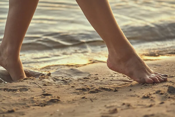 Female feet barefoot on a sandy beach in the water. Close-up of beautiful female legs. Wet foot.