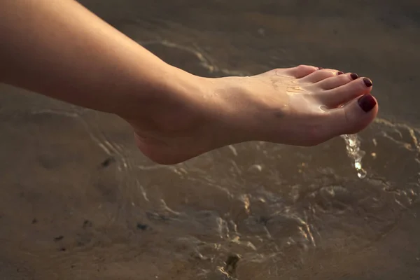 Female feet barefoot on a sandy beach in the water. Close-up of beautiful female legs. Wet foot.