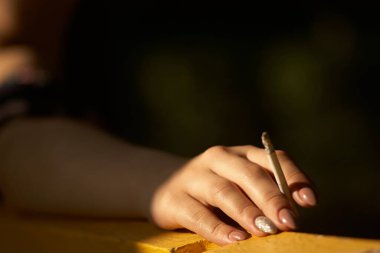 Parkta sigara içen bir kadının yakın çekimi. Umumi bir yerde tütün içme kavramı, sağlığa ve diğerlerine zarar verme, bağımlılık ve kanser.