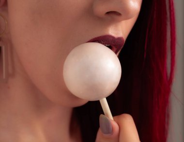 Kadın dudaklarını ve şekerlerini kapat. Çubukta şeker yiyen bir kız. Güzel dudaklar.