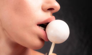 Kadın dudaklarını ve şekerlerini kapat. Çubukta şeker yiyen bir kız. Güzel dudaklar.