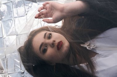 Tombul bir kızın güzel makyajı tül kumaşın altında altın bir folyonun üzerinde yatıyor..