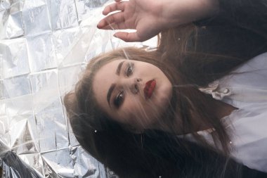 Tombul bir kızın güzel makyajı tül kumaşın altında altın bir folyonun üzerinde yatıyor..