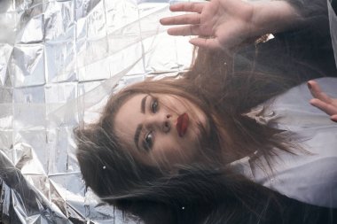 Tombul bir kızın güzel makyajı tül kumaşın altında altın bir folyonun üzerinde yatıyor..