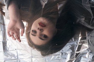 Tombul bir kızın güzel makyajı tül kumaşın altında altın bir folyonun üzerinde yatıyor..